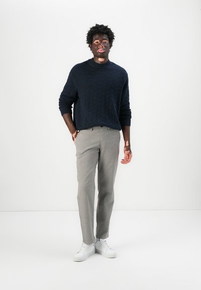 Suéter de punto azul marino con un patrón texturizado, pantalones gris claro y zapatillas blancas. Corte simple y moderno con puños y cintura acanalados.