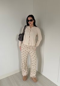 Cardigan beige à boutons, pantalon beige à pois, bottes marron, sac à main noir et lunettes de soleil. Tissu lisse, coupe décontractée et détails de conception subtils.