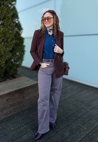 Καφέ σακάκι πάνω από ένα τζιν πουκάμισο, γκρι ψηλόμεσα παντελόνια και μπορντό παπούτσια με μυτερή μύτη. Συμπληρωμένα με oversized γυαλιά ηλίου και έναν scarf.