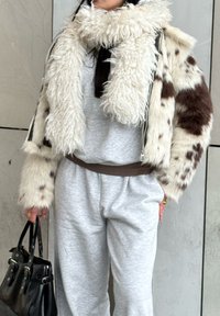 Vilnos imitacijos striukė su baltais ir rudais lopais, pilkas džemperis ir derančios kelnės, derinamos su juoda rankine.