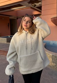 Lys beige fleece hettegenser med stor frontlomme, snor og "ORIGINALS"-tekst. Overdimensjonert passform, myk tekstur og uformelt design.