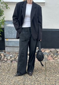 Zwarte oversized blazer, witte aansluitende top, grijze high-waisted broek, polkadot flats en een zwarte handtas. Buiten in een grindomgeving.