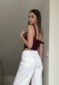 Bordeaux cropped top met brede bandjes gecombineerd met high-waisted witte wijde broekspijpen. De top heeft zijkantknoopsluiting en een gestructureerde afwerking.