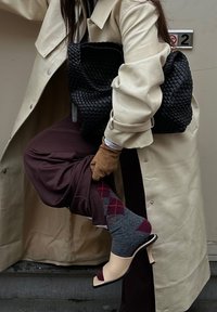 Trench-coat beige, pantalon marron, chaussettes argyle grises et bordeaux, escarpins à bout ouvert rose clair, et sac à main noir tissé texturé.