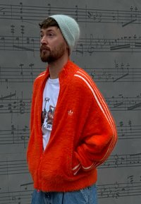 Soft orange zip-up jacket with white stripes down the sleeves, worn over a graphic white t-shirt, paired with blue denim jeans.