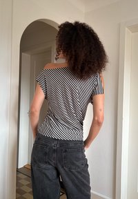 Haut rayé noir et blanc avec un design épaules dénudées, associé à un jean gris foncé taille haute. Le tissu semble doux et légèrement texturé.