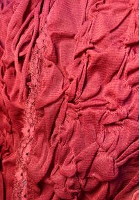 Tissu rouge texturé avec des plis rassemblés créant des motifs tridimensionnels. Matériau doux et léger avec des détails de couture visibles.