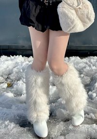 Perneiras brancas de pelúcia falsas combinadas com botas brancas de tornozelo, definidas contra um fundo nevado. Saia curta preta e bolsa combinando estão presentes.