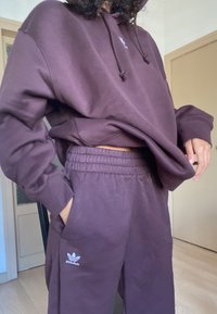 Sudadera morada con cordones y bolsillo tipo canguro en la parte frontal, combinada con pantalones joggers a juego que presentan un logo bordado. Ajuste suave y relajado.
