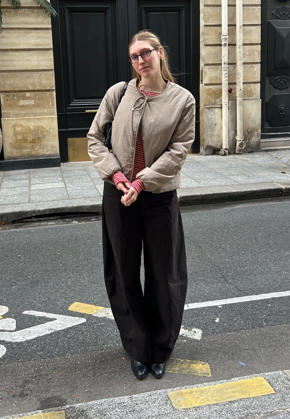 Hellbeige Bomberjacke mit Krawattenverschluss, rot-weiß gestreiftes Oberteil, schwarzhochtaillierte weitgeschnittene Hose und schwarze Stiefeletten.