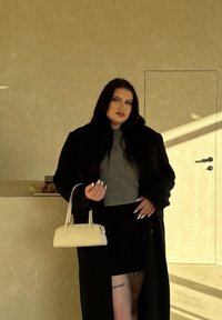 Černý kabát, šedý přiléhavý svetr a černá sukně. Drží malou bílou kabelku. Hladké textury; dlouhé, rovné vlasy. Diskr�étní tetování na stehně.