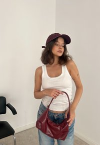 Top de tirantes blanco acanalado, jeans de talle alto azul y un bolso de cuero burdeos. La gorra también es burdeos, con un detalle de lazo en la parte posterior.