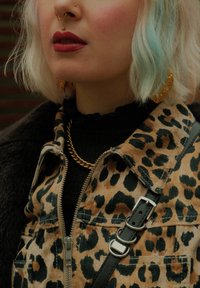 Leopardmønstret kordfløjljakke med grønne detaljer, lagd over en sort top, der har en guldkæde halskæde og store gyldne øreringe.