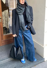 Sort oversized blazer over en sort top, parret med løse blå denimjeans og blå sneakers. Et gråt tørklæde hænger om halsen. Sort taske.