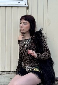 Majica z leopardjim vzorcem z dolgimi rokavi, črne čipkaste kratke hlače, okrašena zelena pas, večplastni perlicni obesek in umetni krzneni šal. Nevtralna ozadja.