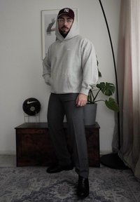 Siv hoodies s sprednjim žepom, sive hlače in črne čevlje. Burgundska bejzbolska kapa, prozorne očala, sobna rastlina in športna žoga v ozadju.
