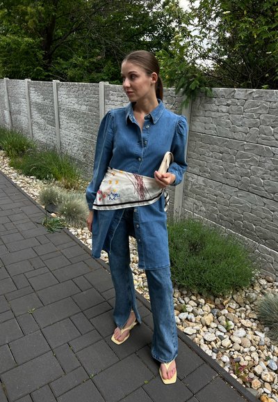 Camisa de denim de manga larga, de corte relajado; combinada con jeans de pierna ancha. Un bolso beige bordado y chanclas amarillas completan el look.