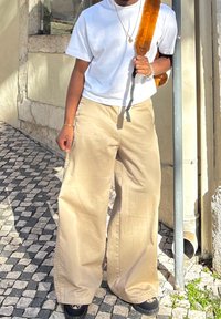 White short-sleeved T-shirt paired with beige wide-leg trousers and black shoes. A brown plush backpack is slung over one shoulder.