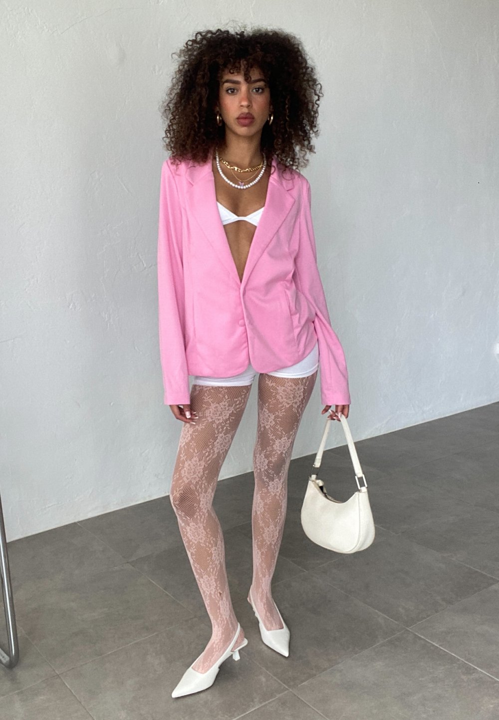 Pink blazer over white top, lace-patterned tights, and white pointed heels. Accessorized with a small white bag and layered necklaces.