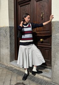 Navy, red and white striped knit sweater, teamed with a white pleated skirt. A woven black handbag and textured black shoes complete the ensemble.