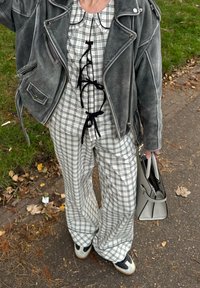 Pelēka zamša motociklistu jaka pār baltu un melnu rūtainu apģērbu ar savilkšanas detaļu. Izskatu papildina pelēka rokas soma un melnbalti sporta apavi.