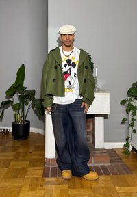 Vihreä villasekoite kaksirivinen takki, valkoinen Mickey Mouse -kuvioinen t-paita, tummat leveälahkeiset farkut, keltaiset puukengät ja kultainen ketju.