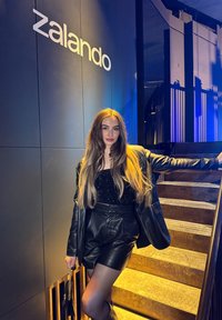 Black leather outfit featuring a sparkly black top and high-waisted shorts, posed next to a modern wooden staircase and the Zalando logo.