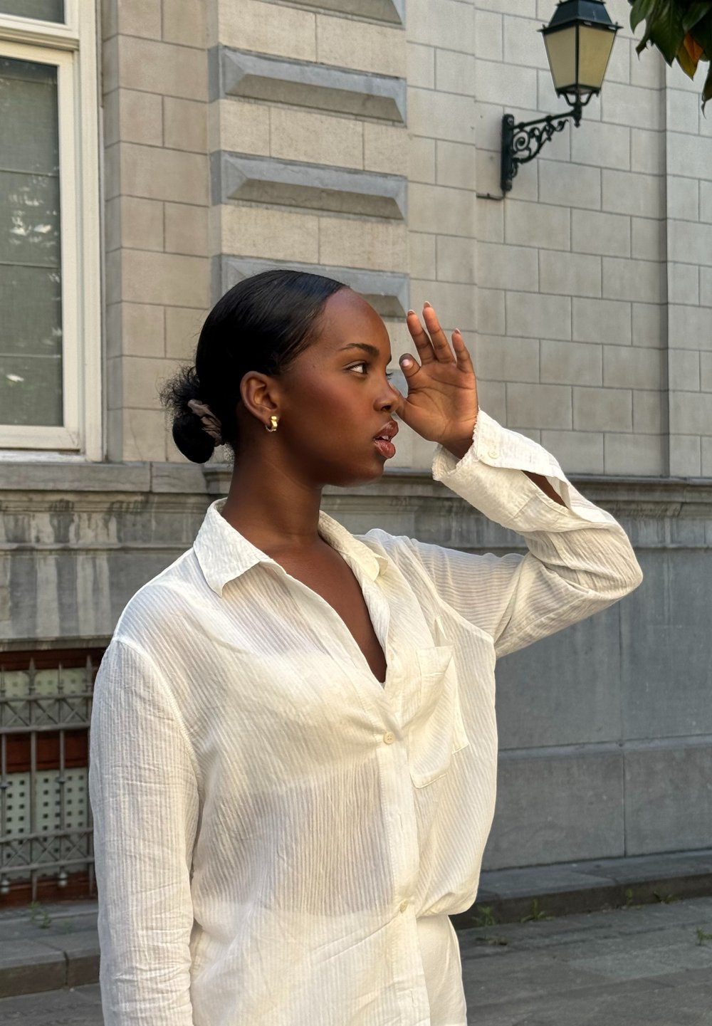 Camicia bianca a righe con vestibilità ampia e tasca, indossata con i capelli raccolti. Completata da orecchini a cerchio dorati.