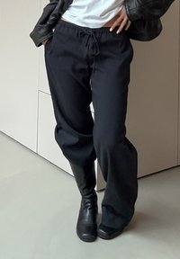 Pantalon noir, ample, en matière légère avec une ceinture élastique et un cordon de serrage. Porte avec des bottes noires montant jusqu'aux genoux.
