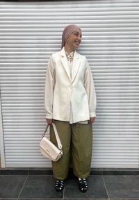 Sacou alb peste un top deschis la culoare, asortat cu pantaloni largi verde măsliniu. Accesoriile includ o geantă crem și sandale negre cu bretele.