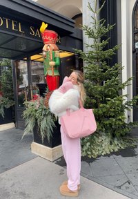 Figurka louskáčka v červené a zelené, načechraný b ílý kabát, světle růžové palčáky, dlouhé růžové kalhoty a růžová taška, s dekoracemi z jehličnatých větviček.