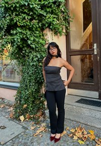 Grey strapless top with a fitted design, paired with black trousers and burgundy high heels. Background features ivy and a door.