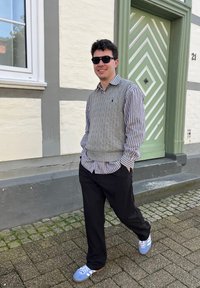 Halliderebe hall nahksulete kudumisvest valgete ja siniste triipudega särgi ning mustade pükste ja siniste tossudega. Seisab rohelise ukse lähedal, millel on kallite mustritega kaunistused.