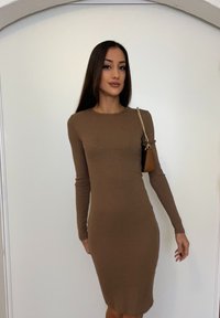 Dopasowana, długosleeve sukienka w ciepłym brązowym prążkowanym materiale. Posiada okrągły dekolt i subtelne rozcięcie po boku. W zestawie z małą brązową torebką.