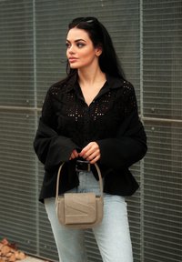 Μαύρο πουκάμισο με κουμπιά και λεπτομέρειες κοπής, σε συνδυασμό με ανοιχτό μπλε τζιν. Γκρίζα τσάντα χειρός με υφασμάτινη καπάκι και γεωμετρικό σχέδιο.