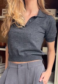 Polo gris charbon à manches courtes avec un col et une patte de boutonnage à trois boutons. Texture douce, porté avec un pantalon gris ajusté.