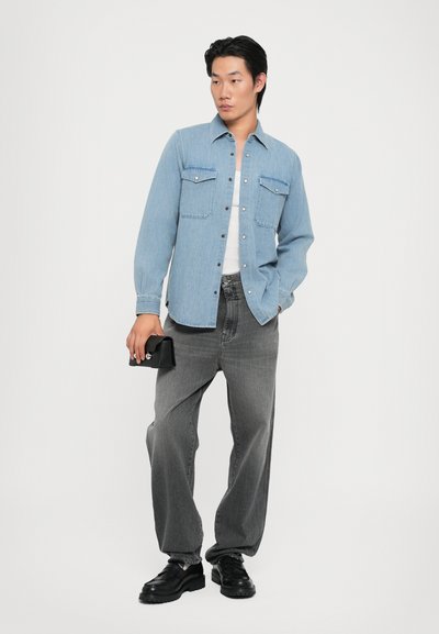 Camisa de mezclilla azul claro con botones y dos bolsillos en el pecho, combinada con jeans grises de corte holgado y zapatos de plataforma negros. LLeva un bolso de mano negro.