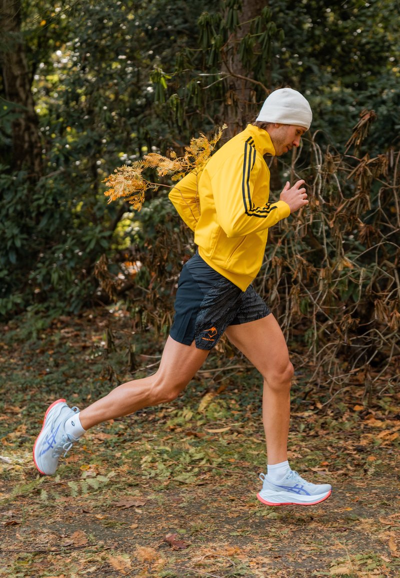 Running shoes with light blue and red accents, paired with black shorts that have a textured pattern and a yellow jacket with black stripes.