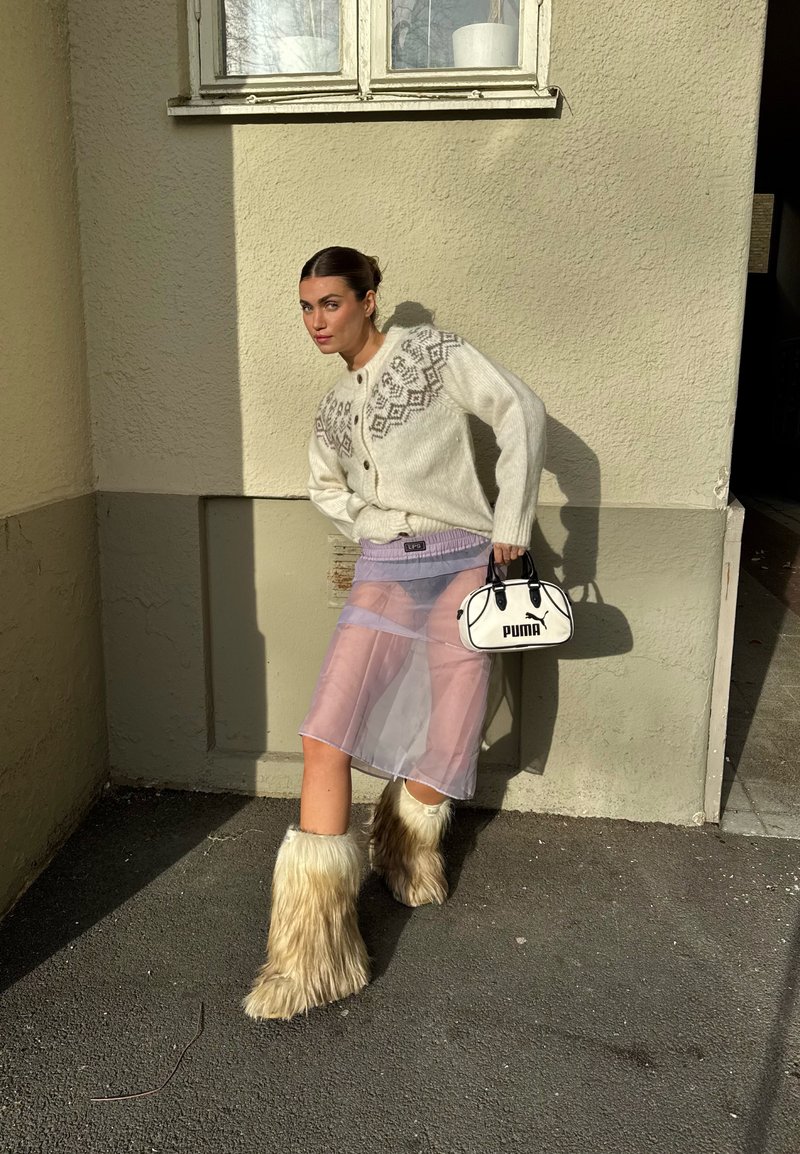 Cardigan creme oversized de malha com padrão Fair Isle cinzento, saia de chiffon lavanda transparente e botas peludas bege; mala preta e branca.