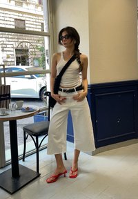 Λευκά κοντά παντελόνια με μπαλώματα στην άκρη, εφαρμοστό λευκό τοπ, και κόκκινες πλατφόρμες με τακούνι. Το μοντέλο κρατάει μια μαύρη τσάντα χιαστί και φοράει γυαλιά ηλίου.