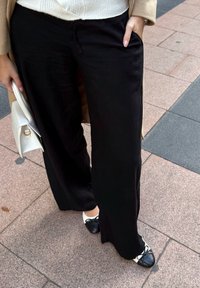 Černé kalhoty s širokými nohavicemi z lehké látky, s postranními kapsami. Kombinovány s černo-bílými lodičkami s mašlí. Viditelná bílá kabelka.