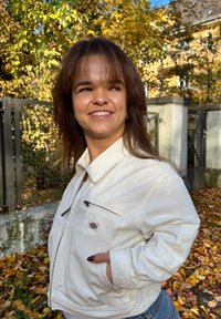 Bela denim jakna z zadrgo, dolgi rokavi in ovratnik. Nosljena preko modrih kavbojk, postavljena na ozadju jesenskih listov.