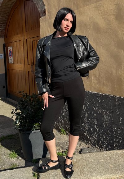 Chaqueta de cuero negra de motociclista sobre una blusa negra ajustada, combinada con leggings negros cortos y zapatos negros con tiras y acentos metálicos.