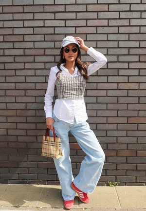 Top corto a cuadros grises sobre una camisa blanca de botones, jeans acampanados de un azul claro, zapatillas rojas, gafas de sol y una bolsa de cuadros.