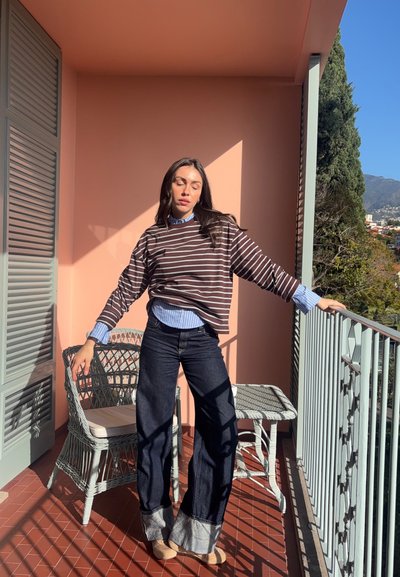 Suéter de gran tamaño a rayas marrones y blancas sobre una camisa de cuello azul claro, combinado con jeans flare oscuros que tienen acentos de puño en azul claro.