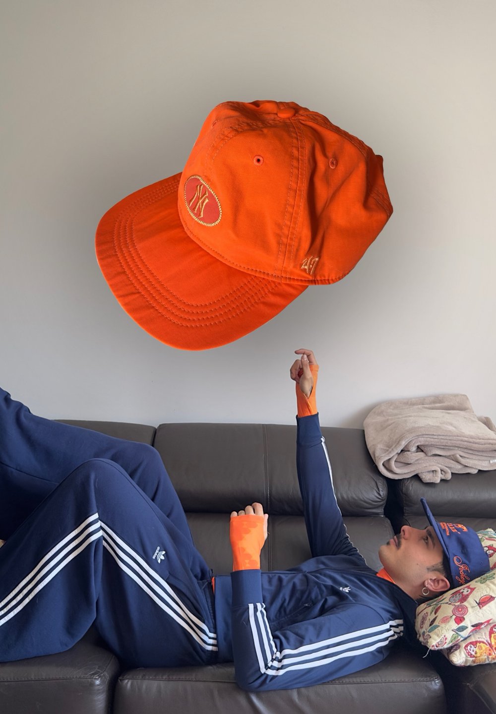Cappellino da baseball arancione con logo ricamato, materiale in cotone, visiera curva e cinturino regolabile sul retro, posizionato sopra una persona in tuta blu.