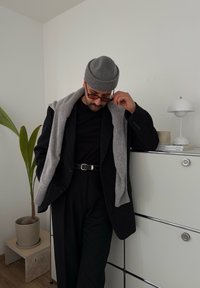 Μαύρο μαλλίνη παλτό πάνω από ένα μαύρο μπλουζάκι, γκρι κασκόλ ριγμένο στους ώμους, γκρι πλεκτό σκουφί, γυαλιά ηλίου και μαύρη ζώνη με ασημένια αγκράφα.