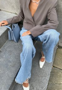 Grijze oversized blazer, lichtblauwe versleten jeans, witte puntige schoenen en een kleine grijze tas. Zachte texturen met rafelige jeansranden.