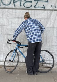 Vélo de route bleu avec des pneus noirs et un cadre élégant. Une personne portant une chemise à carreaux bleue et un pantalon foncé ajuste le guidon.