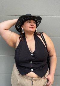 Schwarzes Leinentop mit V-Ausschnitt und dekorativen Knöpfen, kombiniert mit beigen gestreiften Hosen. Schwarzer geflochtener Hut und Creolen.